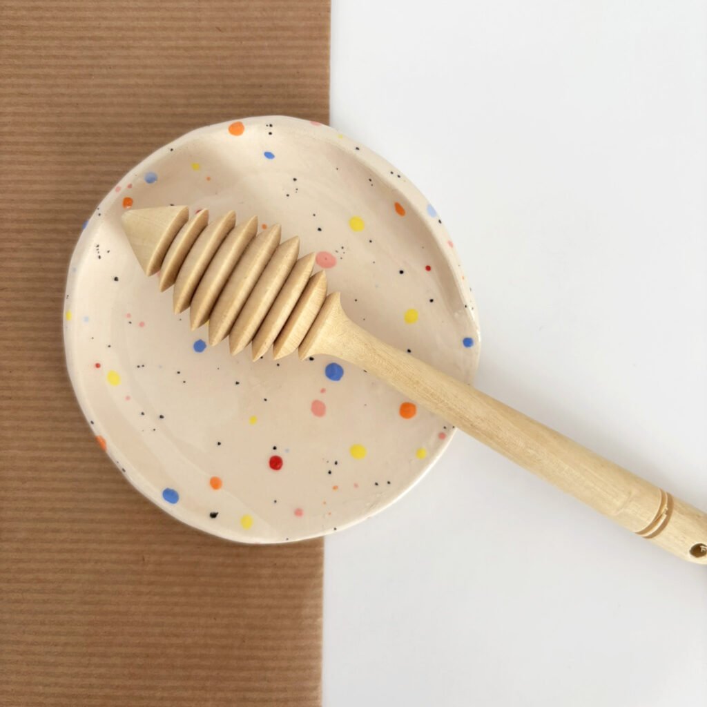 Repose-cuillère en céramique blanche parsemée de confettis colorés, avec une cuillère à miel en bois